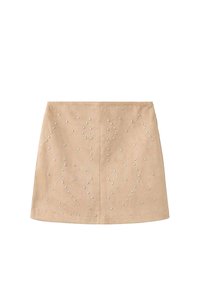 Falda beige de ante adornada con tachuelas decorativas de plata de varios tamaños, con una forma ceñida y dobladillo recto.