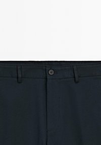 Pantalon gris foncé à la texture lisse, doté d'une fermeture à bouton et de passants de ceinture. La taille est légèrement élastiquée pour un maximum de confort.