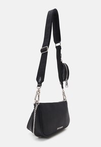 Černá texturovaná kabelka přes rameno se stříbrným řetízkovým detailem, nastavitelným širokým popruhem a malou kulatou zipovou kapsičkou připevněnou k popruhu.