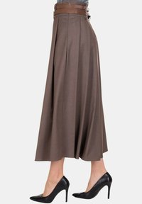 Gonna midi marrone a vita alta abbinata a una cintura larga, indossata con décolleté nere con punta affilata su sfondo bianco.