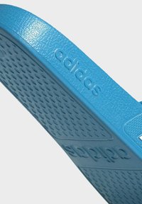 Blauwe Adidas-sandaal met een gestructureerde rubberen zool, met reliëfmerknaam, platte ontwerp en brede banden.