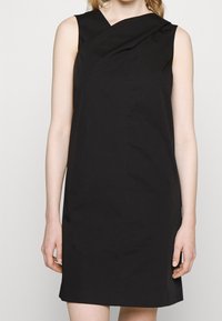 Černé šaty bez rukávů s designem zakřiveného ramene, vyrobené z hladkého materiálu, s přiléhavým siluetou a délkou ke kolenům.
