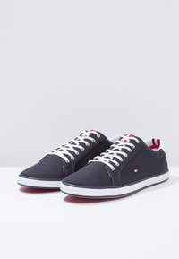 Sneakers in tela blu navy con lacci bianchi e suole in gomma. Presentano dettagli rossi e blu sulla linguetta e un piccolo logo di lato.