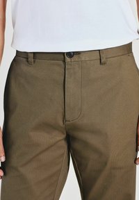 Pantalons texturés marron avec coupe droite, dotés d'un bouton de fermeture à l'avant, de passants de ceinture et de poches latérales.