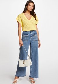 Top giallo a maglia con scollo a V, abbinato a jeans a gamba larga di un blu chiaro a vita alta e una borsa bianca con dettagli dorati.
