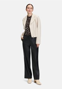 Svetle béžová zkrácená bunda s klopami, černý vzorovaný top a černé široké kalhoty z umělé kůže. Béžové kotníkové boty doplňují outfit.