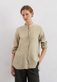Beige linen shirt with a mandarin collar, long sleeves rolled at the cuffs, and button closure down the front; relaxed fit.