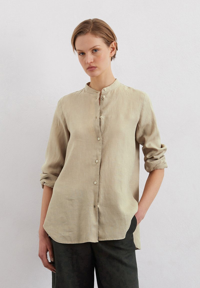 Beige linen shirt with a mandarin collar, long sleeves rolled at the cuffs, and button closure down the front; relaxed fit.