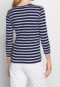 Morsko-niebieska i biała w paski bluzka z długim rękawem, okrągłym dekoltem i dopasowanym krojem, wykonana z miękkiego, elastycznego materiału.