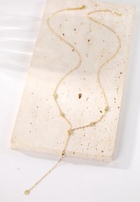 Goldene Halskette mit herzförmigen Akzenten und funkelnden Steinen, ausgestattet mit einer zarten Kette und einem Tropfendesign, das auf einer hellen Steinoberfläche ruht.