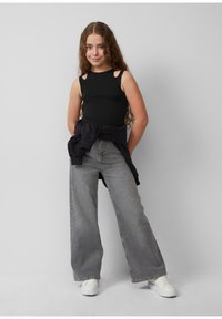 Czarny top bez rękawów z wycięciami na ramionach, poł�ączony z szarymi, szerokimi spodniami z wysokim stanem. Obuwie to białe trampki. Stylizacja na co dzień.