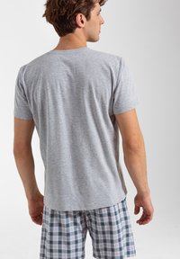 Szara koszulka z krótkim rękawem i okrągłym dekoltem, w zestawie z piżamowymi szortami w kratę w kolorach białym, niebieskim i zielonym. Wykonana z miękkiej bawełny.