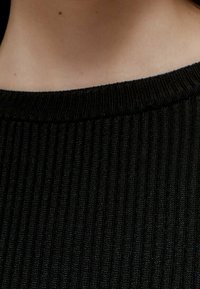 Sort ribstrikket stof med en tætsiddende halsudskæring, der viser en fin tekstur og ensartede lodrette striber.