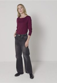 Burgundy long-sleeve top paired with black wide-leg jeans. The outfit features a smooth texture and a relaxed fit, complemented by black boots.