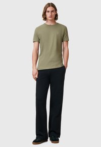 T-shirt in cotone verde oliva con collo rotondo e maniche corte, abbinata a pantaloni neri larghi e scarpe nere con suole marroni.