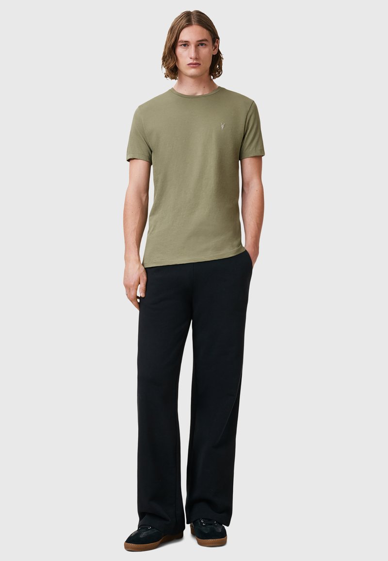 T-shirt in cotone verde oliva con collo rotondo e maniche corte, abbinata a pantaloni neri larghi e scarpe nere con suole marroni.