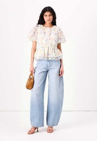 Hvit blomstrete peplum-top med korte pufferm, sammen med lyseblå vide jeans. Tilbehør med en liten brun håndveske.