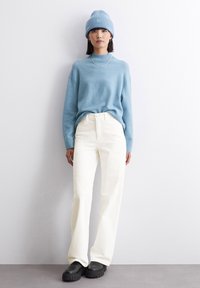 Pulover tricotat de culoare albastru deschis, pantaloni albi cu talie înaltă și pantofi cu platformă negri. Modelul poartă o căciulă din tricot în ton cu puloverul și o bijuterie din metal argintiu.