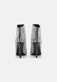 Bottes noires à la cheville recouvertes de grands rhinestones argentés, avec un talon haut élégant et une texture lisse, dotées d'un design à bout rond.