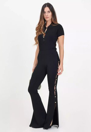 Schwarzer Jumpsuit mit kurzen Ärmeln, hoher Taille und ausgestellten Beinen. Verfügt über Knopfakzente entlang der seitlichen Schlitze, aus dehnbarem Stoff gefertigt.