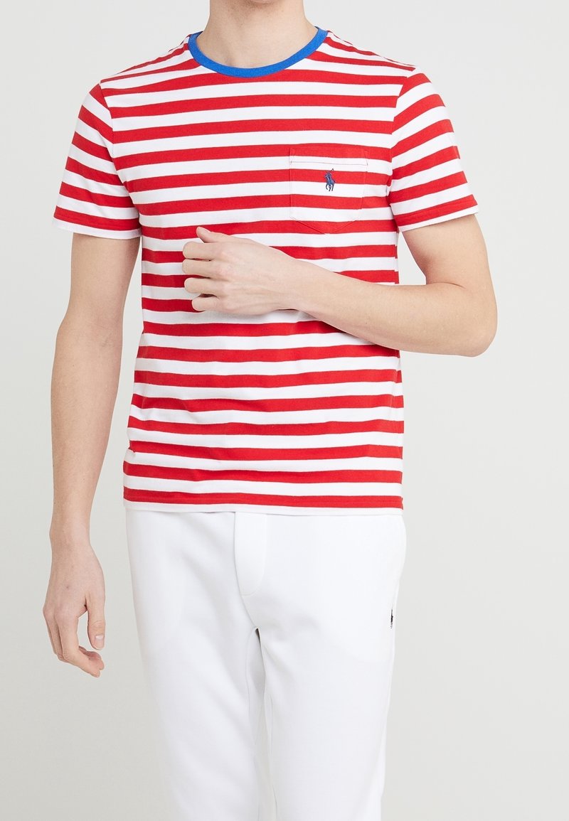 červeno-bílý pruhovaný tričko s krátkým rukávem a modrým žebrovaným límcem, s kapsou na levé hrudi. Má malou logo nad kapsou.