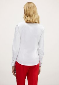 Camisa blanca de manga larga con una silueta suave, que presenta puños abotonados. Combinada con pantalones rojos, que muestran un esquema de color contrastante.