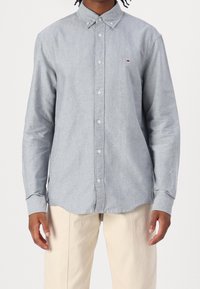 Ljust grå långärmad skjorta med knappar i mjukt tyg, med en button-down krage och en liten logotyp på bröstet.