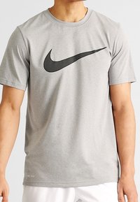 Grå kortärmad Nike T-shirt i andasvänligt material, med en stor svart swoosh-logotyp över bröstet och "DRI-FIT"-detalj vid fållen.