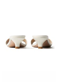 Paire de sandales mule blanches à petit talon, vues de dos sur fond blanc, avec orteils ouverts et talons texturés.