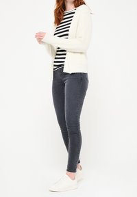 Vit stickad cardigan över en svartvit randig topp, matchad med mörkgrå skinny jeans och vita sneakers. Enkel och avslappnad outfit.