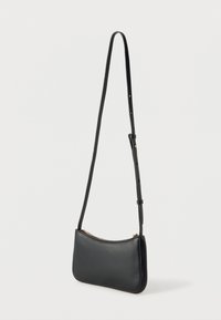 Μαύρο δερμάτινο τσάντα μέσης με χρυσό φερμουάρ και ρυθμιζόμενο μακρύ λουρί κρεμασμένο σε λευκό φόντο.