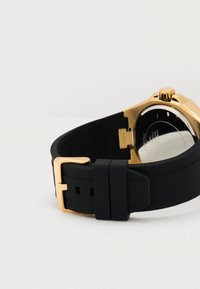 Cinturino per orologio in gomma nera con fibbia dorata, dotato di una cassa metallica e un retro liscio, che enfatizzano un design moderno e la durata.