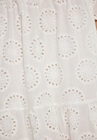 Bílý bavlněný textil s vyšívanými kruhovými vzory a detailem vyřezávání. Má měkkou texturu s vrstvenými designovými prvky.