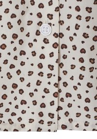 Beiges Gewebe mit einem Leopardenmuster in Braun und Schwarz, ausgestattet mit einem weißen Vierlochknopf, der nahe der Mitte angenäht ist.