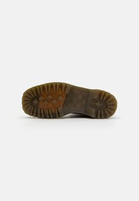 Suela de bota de goma con surcos profundos para tracción. Color marrón con un acabado texturizado y un logo distintivo. Diseño minimalista, construcción robusta.