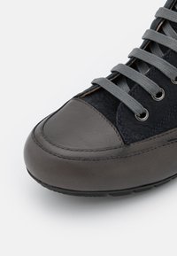 Sneaker grigio e nero con una punta in pelle liscia, pannelli laterali testurizzati, lacci grigi e occhielli in metallo, caratterizzato da dettagli cuciti.