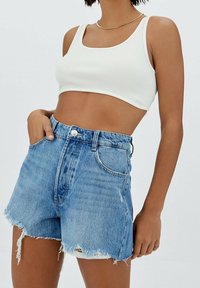Valkoinen ribbed crop-top, joka on yhdistetty korkeavyötäröisiin farkkushortsit. Shortsit ovat vaaleansiniset, päällipuoli kuluneita ja lievästi rikkinäisiä, viiden taskun muotoilu.