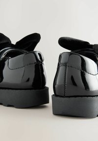 Schwarze Lacklederschuhe mit einer glatten, glänzenden Oberfläche und runder Zehenform, ausgestattet mit einer strukturierten schwarzen Gummisohle und weichen Stoffakzenten.