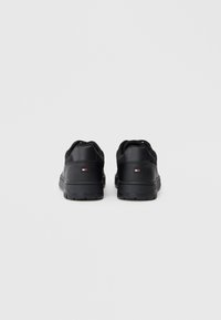Czarne sneakersy z gładką syntetyczną cholewką, wyściełanym kołnierzem i teksturowaną gumową podeszwą. Zawierają małą metkę z logo na pięcie.