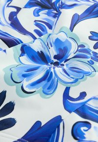 Zbliżenie materiału z niebiesko-białym wzorem kwiatowym, zawierającym duże płatki i wirujące liściaste motywy na jasnym tle.