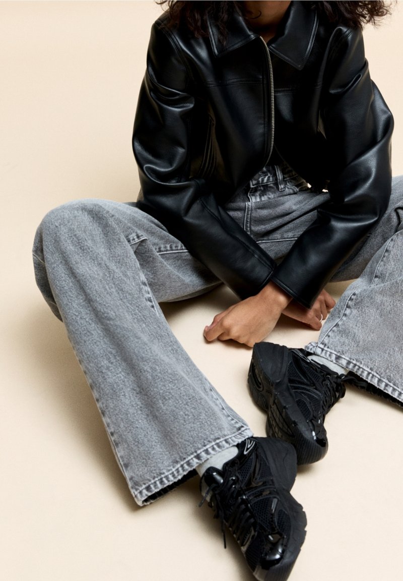 Black leather zip-up jacket, light gray wide-leg jeans, and chunky black sneakers. Smooth texture and modern design with detailed stitching.