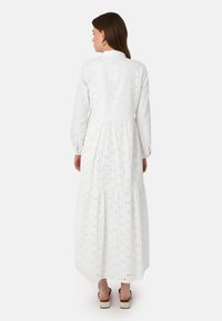 White long-sleeve dress with textured eyelet pattern, round neckline, tiered skirt, and gathered waist. Floor-length with a flowy silhouette.