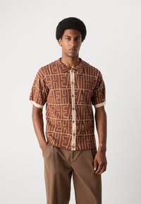 Short-sleeve shirt in brown knit fabric with large light beige lettering. Features a collar, button front, and contrasting cuff details.