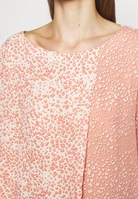 Blusa ligera con una combinación de colores en rosa y crema, con patrones texturizados y en relieve. Diseño de cuello barco y corte relajado.