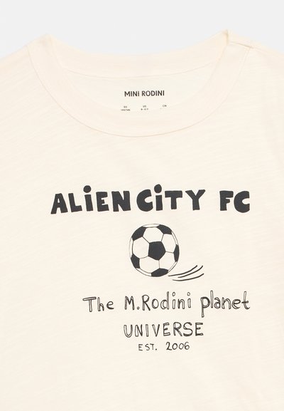 Κρεμ πουκάμισο με μαύρο κείμενο "ALIEN CITY FC," γραφικό μαύρο-άσπρης ποδοσφαιρικής μπάλας και τη φράση "The M. Rodini planet UNIVERSE EST. 2006."