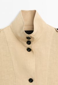 Beige high-collar jacket with vertical seams and four black buttons fastened at the front.
