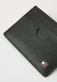 Black leather cardholder with textured surface, featuring multiple card slots and a small logo in a rectangular design at the bottom corner.