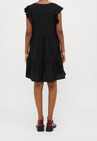 Svart, lager-på-lager klänning med volangärmar, tillverkad av ett lätt material. Matchad med glänsande röda skor med tjock klack i svart.