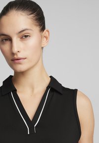 Polo negro sin mangas con un collar, escote en V y ribete blanco en contraste a lo largo del escote para un aspecto limpio y moderno.