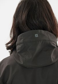 Mörkgrön vattentät jacka med hög krage, försedd med en liten logotyp på baksidan och en jämn, matt textur.